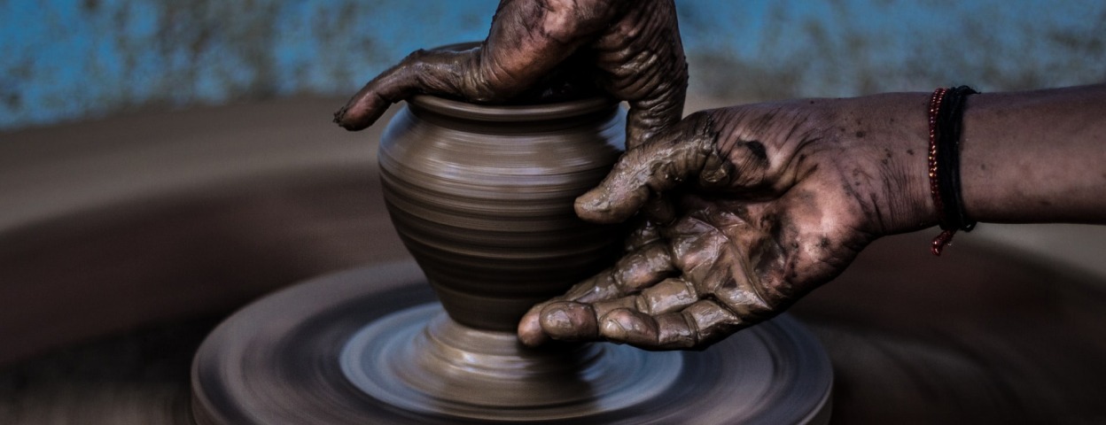 A person with a dark skin tone shaping a clay vase on a throwing wheel
